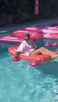 Person lounging on a pink inflatable ring in a pool with other inflatables.