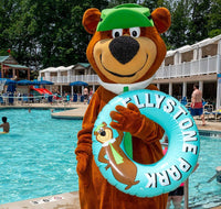 Mascot character holding a 'Yosemite National Park' floatie by a pool with people in the background.