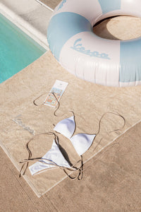 White bikini on a towel next to a pool with a branded inflatable ring.