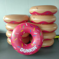 Inflatable donut rings with colorful sprinkles and 'Dunkin' branding on a gray floor.