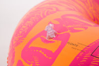 Close-up of a pink and orange inflatable pool float with brand name on a light gray background