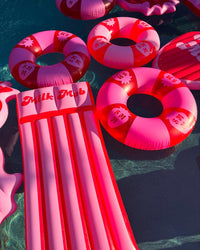 Pink inflatable pool floats with 'Milk Mob' branding on a dark water surface.