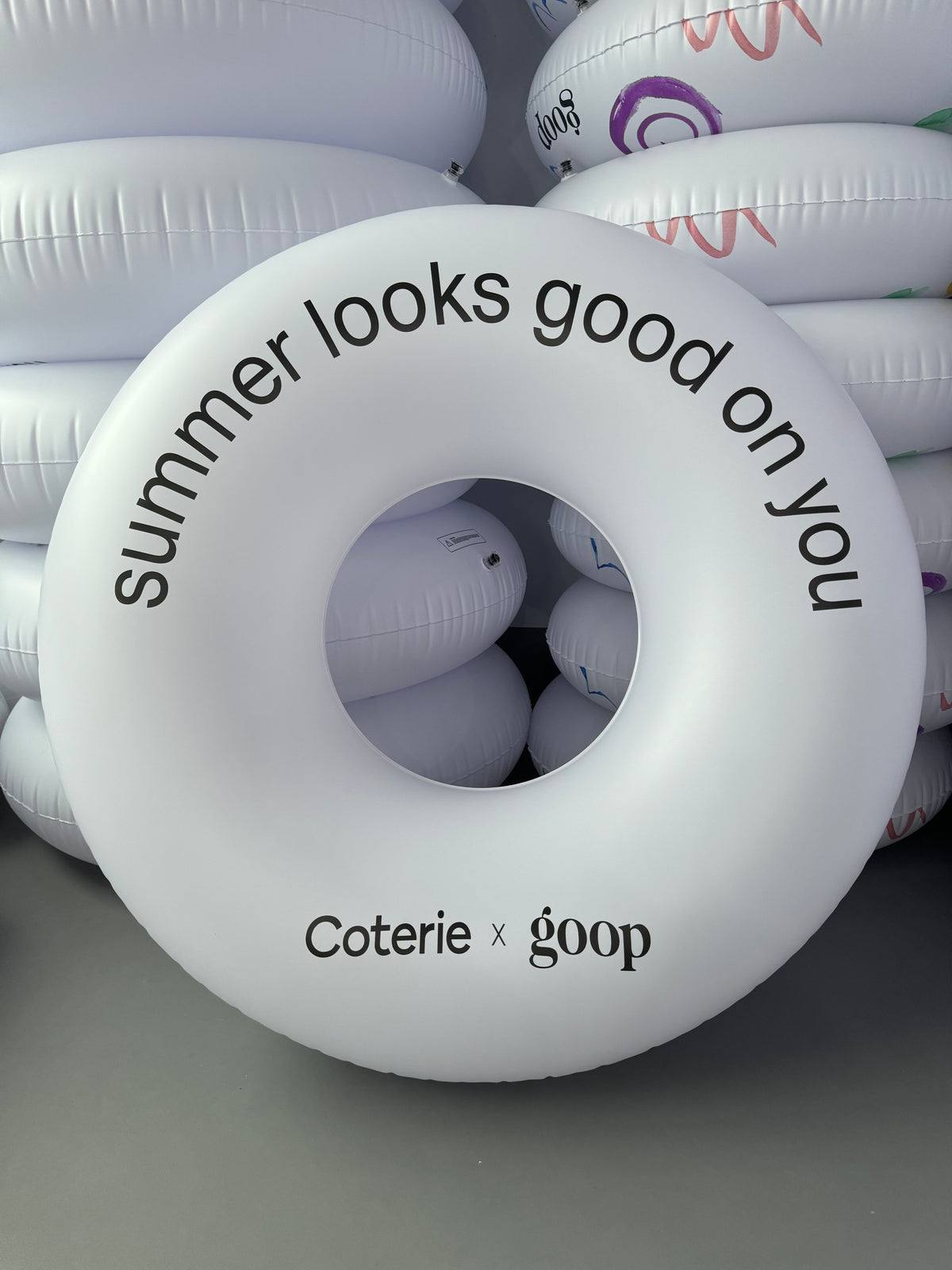 White inflatable ring with text 'summer looks good on you' and 'Coterie x goop' branding.